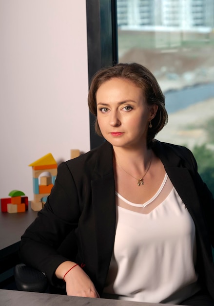 Confident young adult business woman with loose brown hair in black suit with professional make up trendy wavy hairdo and perfect skin Caucasian beautiful brunette model at work in the office