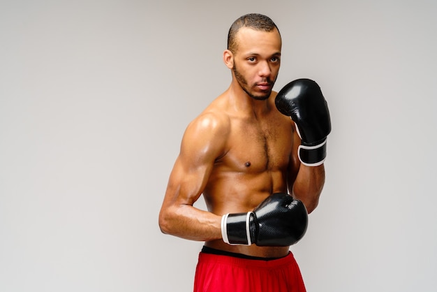 Confident young African boxer in boxing gloves standing over light grey wall