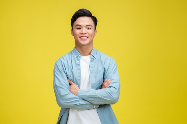 Confident young asian man standing cross arms against yellow background