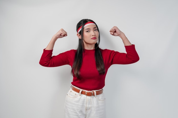 Photo confident young asian woman in a red shirt and white pants raising her arms and muscles