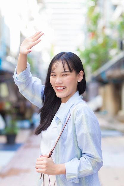 Confident young Asian woman who wears blue white shirt , bag she raised her hand to block sunlight