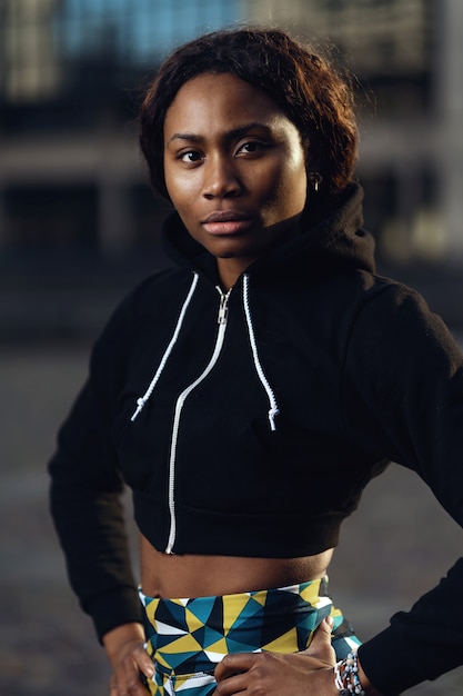 Confident young black african sporty woman portrait outdoors with dramatic light.