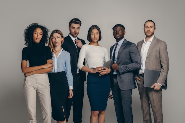 Confident young business people looking at camera while standing on beige background together