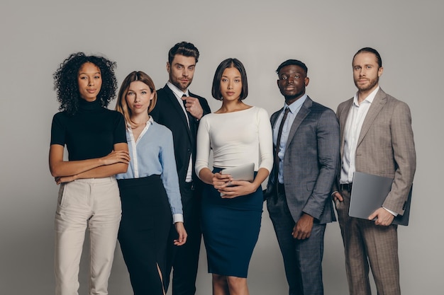 Confident young business team looking at camera while standing on beige background together