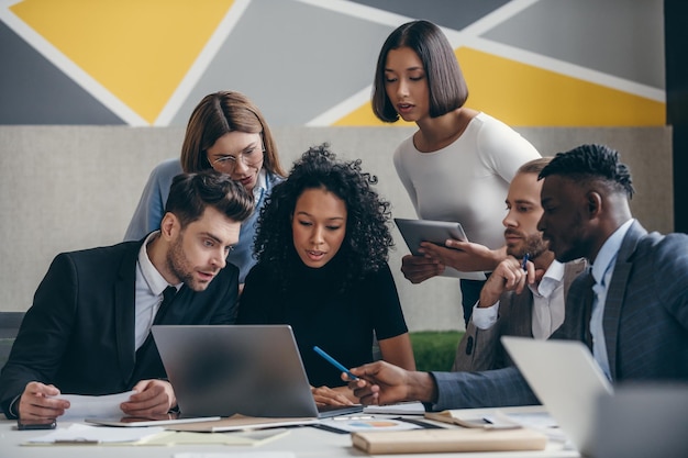 Confident young business team looking at laptop while having group meeting in the office together