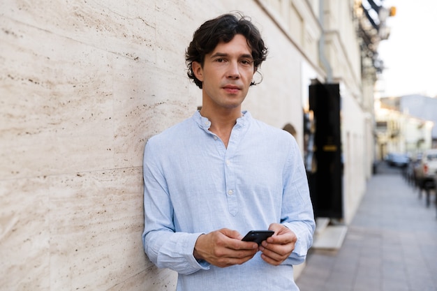 Confident young casual man holding mobile phone