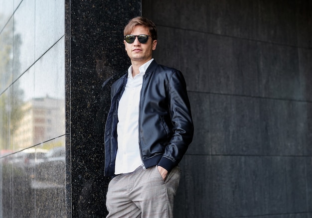 Confident young handsome business man wearing sunglasses, posing outside near building.