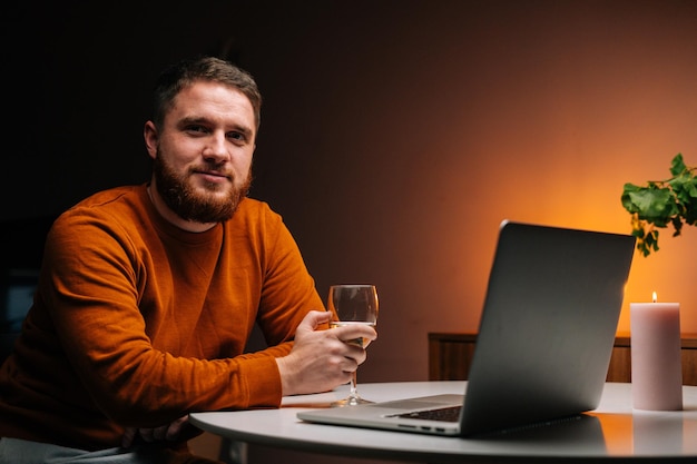 Confident young man enjoying distant dating using laptop computer holding glass with champagne talking celebration toasting via video call