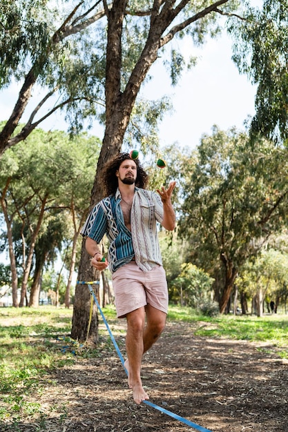 Confident young man juggling and balancing on the slackline in city park