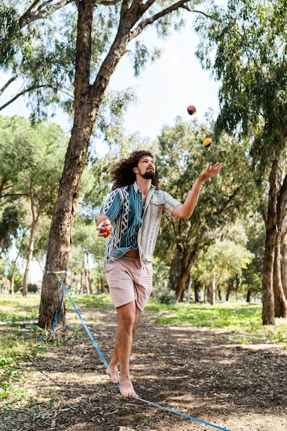 Confident young man juggling and balancing on the slackline in city park