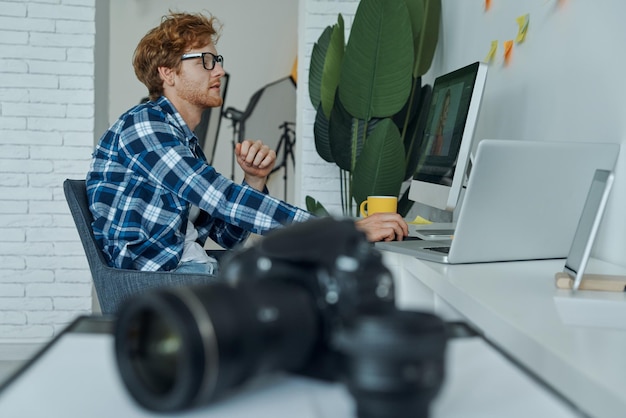 Confident young man using computer while digital camera laying on foreground