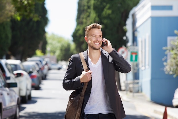 Confident young man walking outside with mobile phone