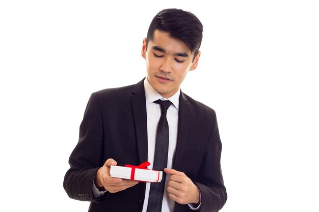 Confident young man with black hair in white shirt and black suit with tie holding a present