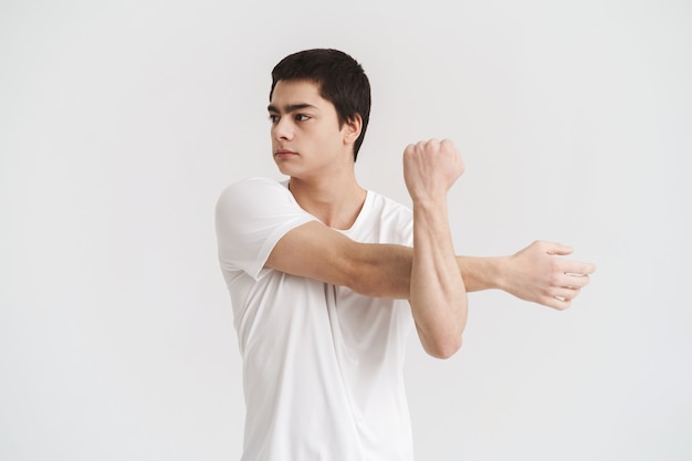 Confident young sportsman doing stretching exercises isolated over white wall