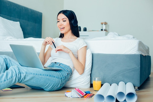 Confident young woman improving her skills by taking online course in graphic design Drawings and color pallets on the floor by her side