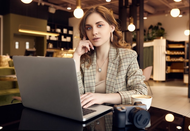 Confident young woman photographer in smart casual wear working on laptop