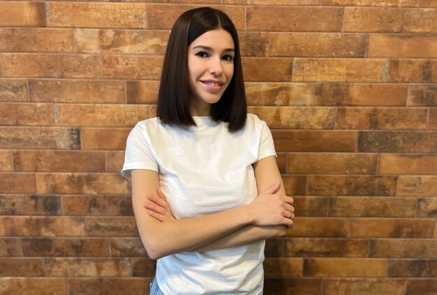 Confident young woman posing with arms crossed against brick all background