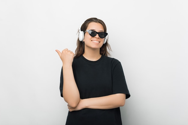 Confident young woman with arms crossed is pointing with thumb aside.