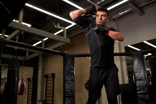 Confidently Looking Male In Black Wear Looking Forward Preparing For Fighting, Wearing Gloves. Sport, Fitness, Boxing Concept