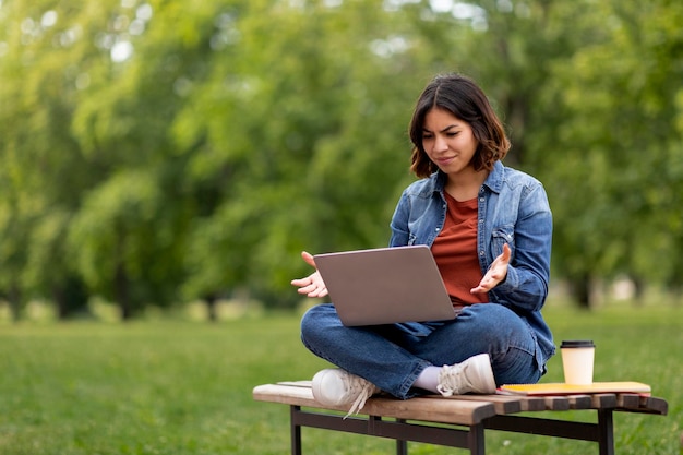 Confused arab woman having problem with laptop while sitting on bench outdoors