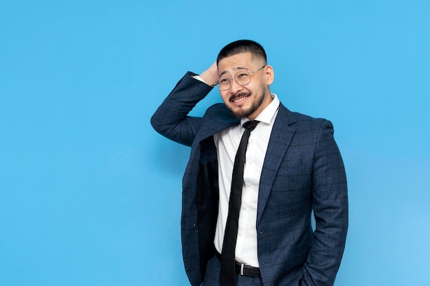 Confused asian businessman in suit and glasses remembers on blue isolated background