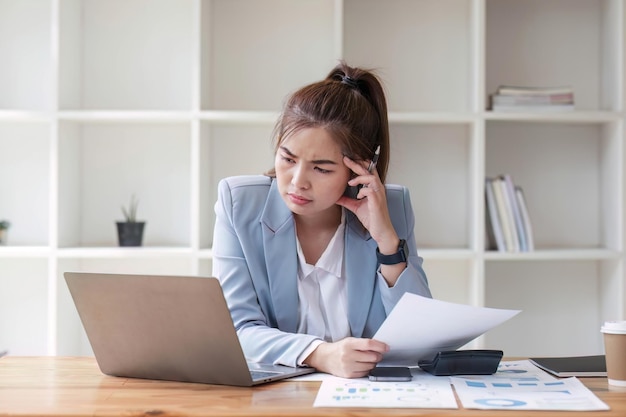 Confused Asian woman thinking hard about how to solve problems online looking at laptop screen Serious Asian businesswoman worried focused on solving difficult computer at office