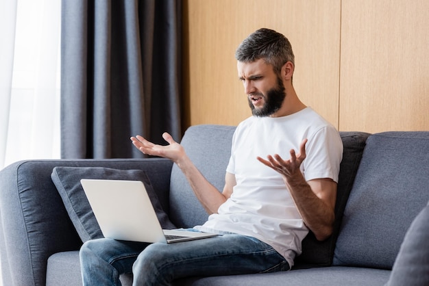 Confused freelancer looking at laptop while sitting on couch at home