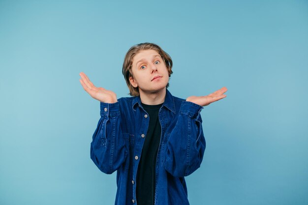 Confused guy in a blue shirt stands on a blue background and looks puzzled at the camera