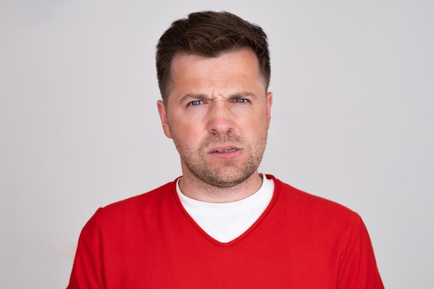 Confused guy wearing red tshirt waiting news looking at camera with doubt