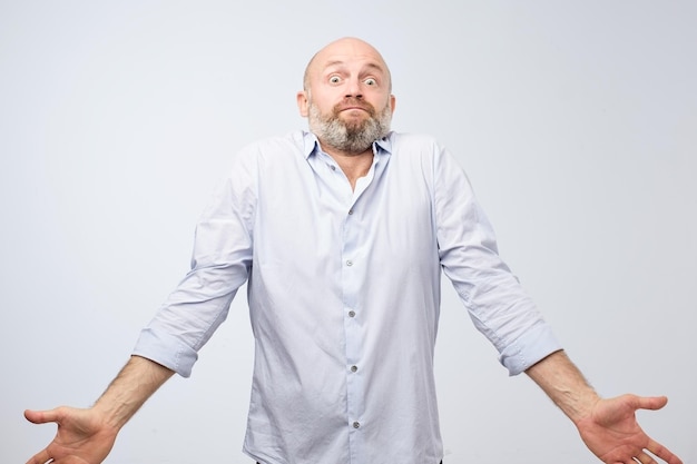 Confused mature bearded man standing and shrugging shoulders isolated over white background