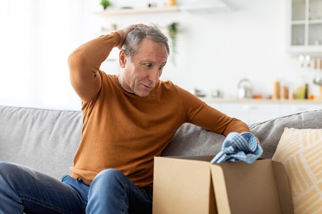 Confused mature man unpacking wrong parcel delivery mistake concept