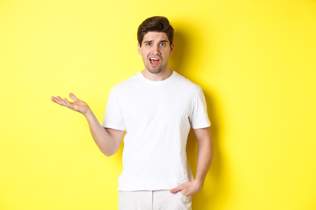 Confused and shocked man complaining, raising one hand and looking bothered, standing near yellow.