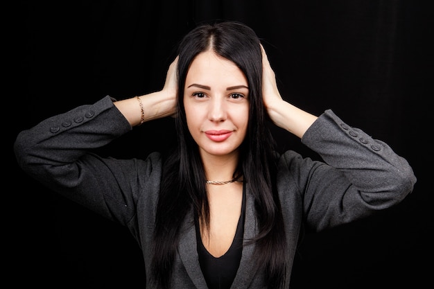 Confused woman holding hands on head over black studio background. Portrait of young serious girl closing her ears, hear no evil, deafness concept, copy space.