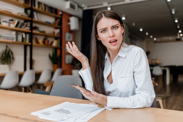 Confused woman in the office with phone and papers