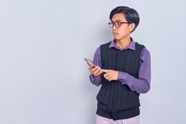 Confused young Asian man in casual shirt using smartphone and looking away at copy space isolated on white background People lifestyle concept