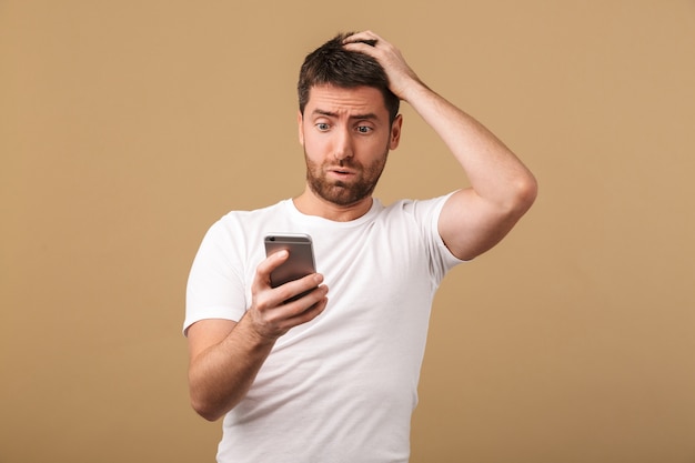 Confused young casual man holding mobile phone isolated