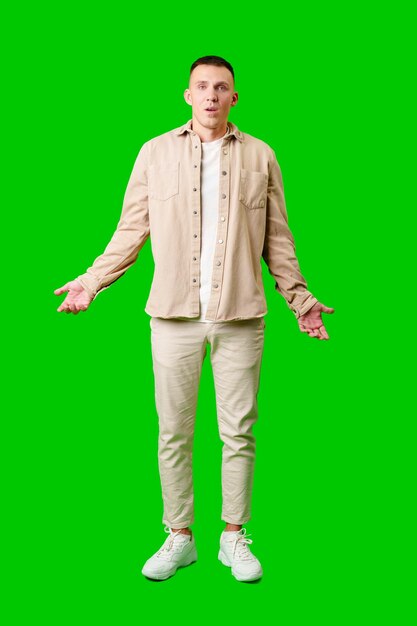 Photo confused young man standing against bright green background with open arms in uncertain gesture