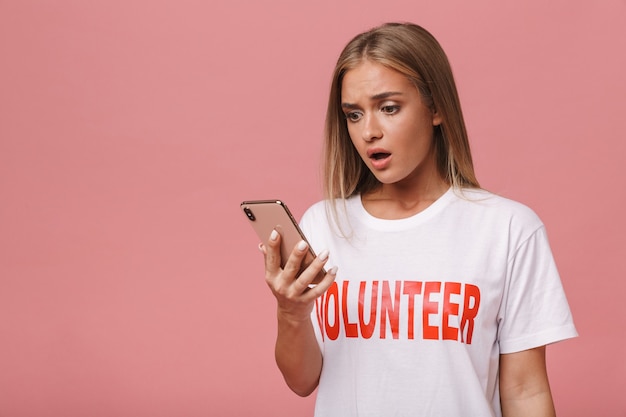 Confused young volunteer girl standing isolated, using mobile phone