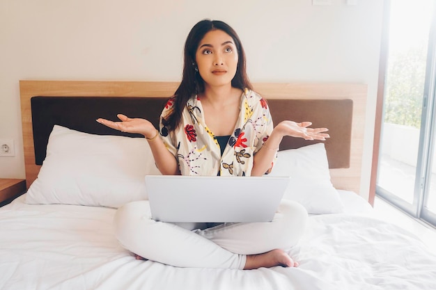 Confused young woman working from the bed Hold the laptop on the knees and type on the keyboard