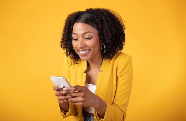 Connected and content happy black lady using smartphone and smiling chatting with guys yellow