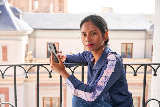 Connected and Entertained Young Indian woman enjoys her phone while sitting on the windowsill