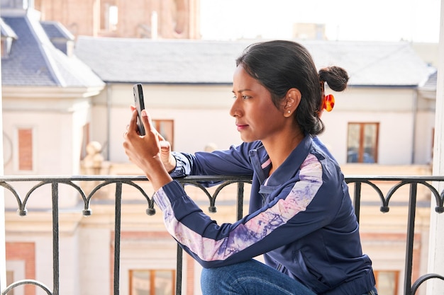 Connected and Entertained Young Indian woman enjoys her phone while sitting on the windowsill