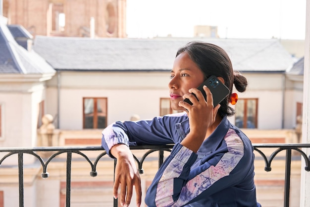 Connected and Productive Young Indian woman multitasks on her phone while sitting on the windowsill