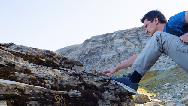 To conquer the mountains a young man travels in the mountains climbs on a rock closeupstep wide