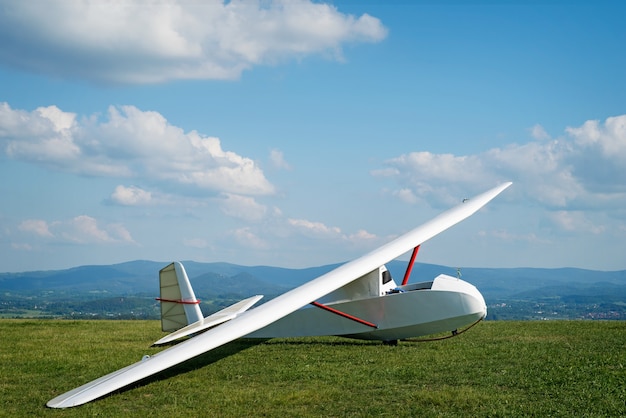 Conquer the world, sunny day, blue sky, on green field stand white glider ready to fly.