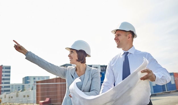 construction, architecture, business, teamwork and people concept - happy architects with blueprint at building site