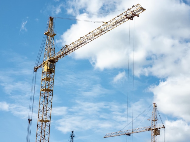 Construction concept. Tower cranes against a bright blue sky with clouds. Horizontal photo.