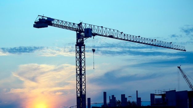 Construction cranes with built houses on the background of the sunset sky