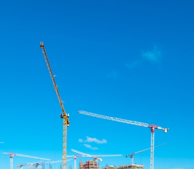 Construction cranes work on creation site against blue sky background Bottom view of industrial crane Concept of construction of apartment buildings and renovation of housing Copy space