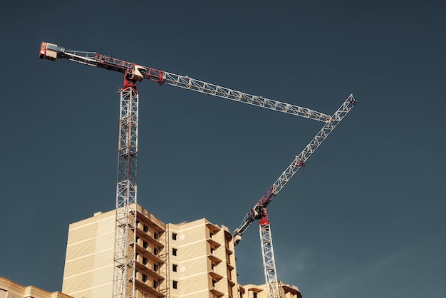 Construction cranes work on creation site against sky background